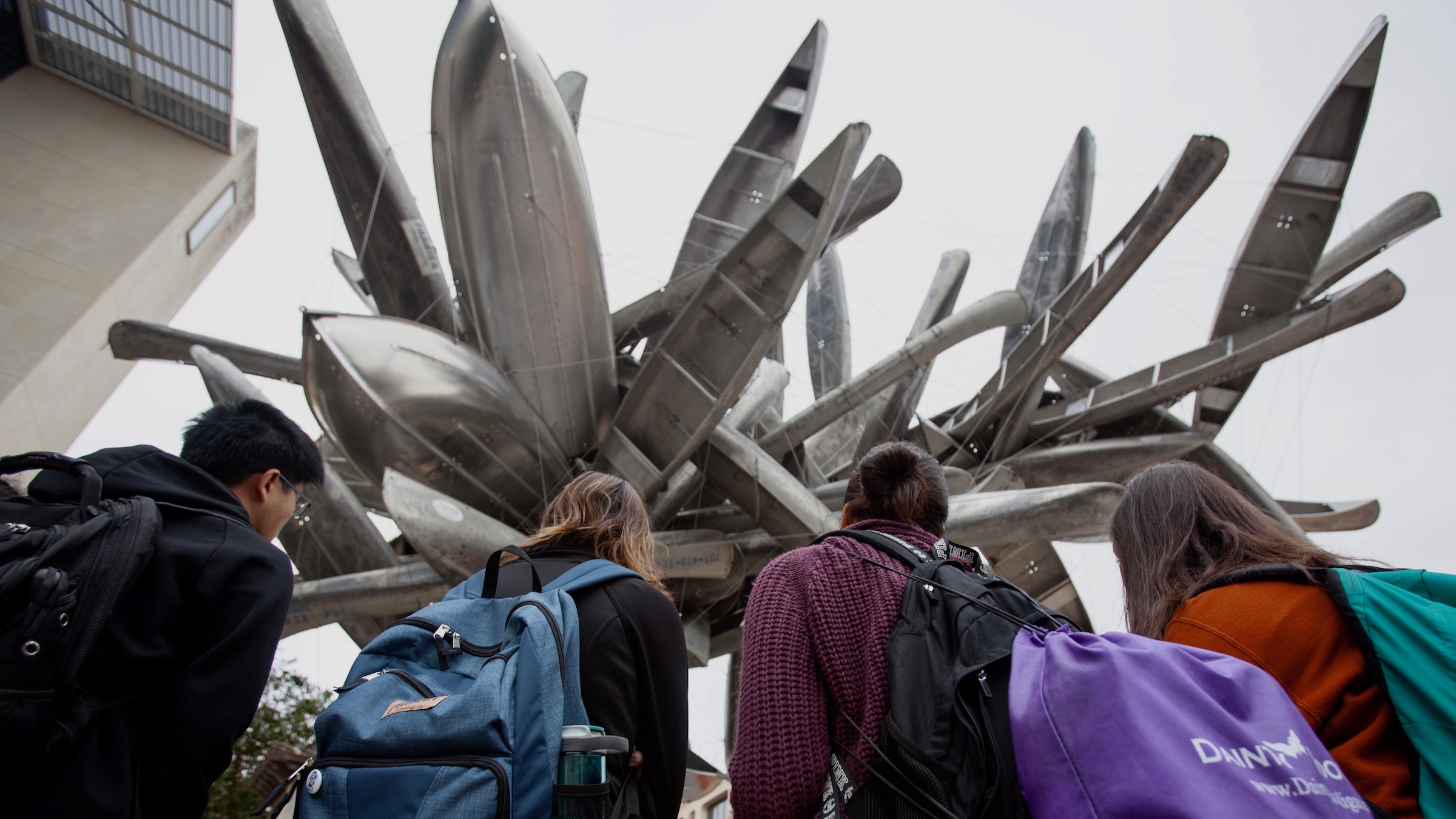 group of four students looking at an outdoor sculpture made of boats