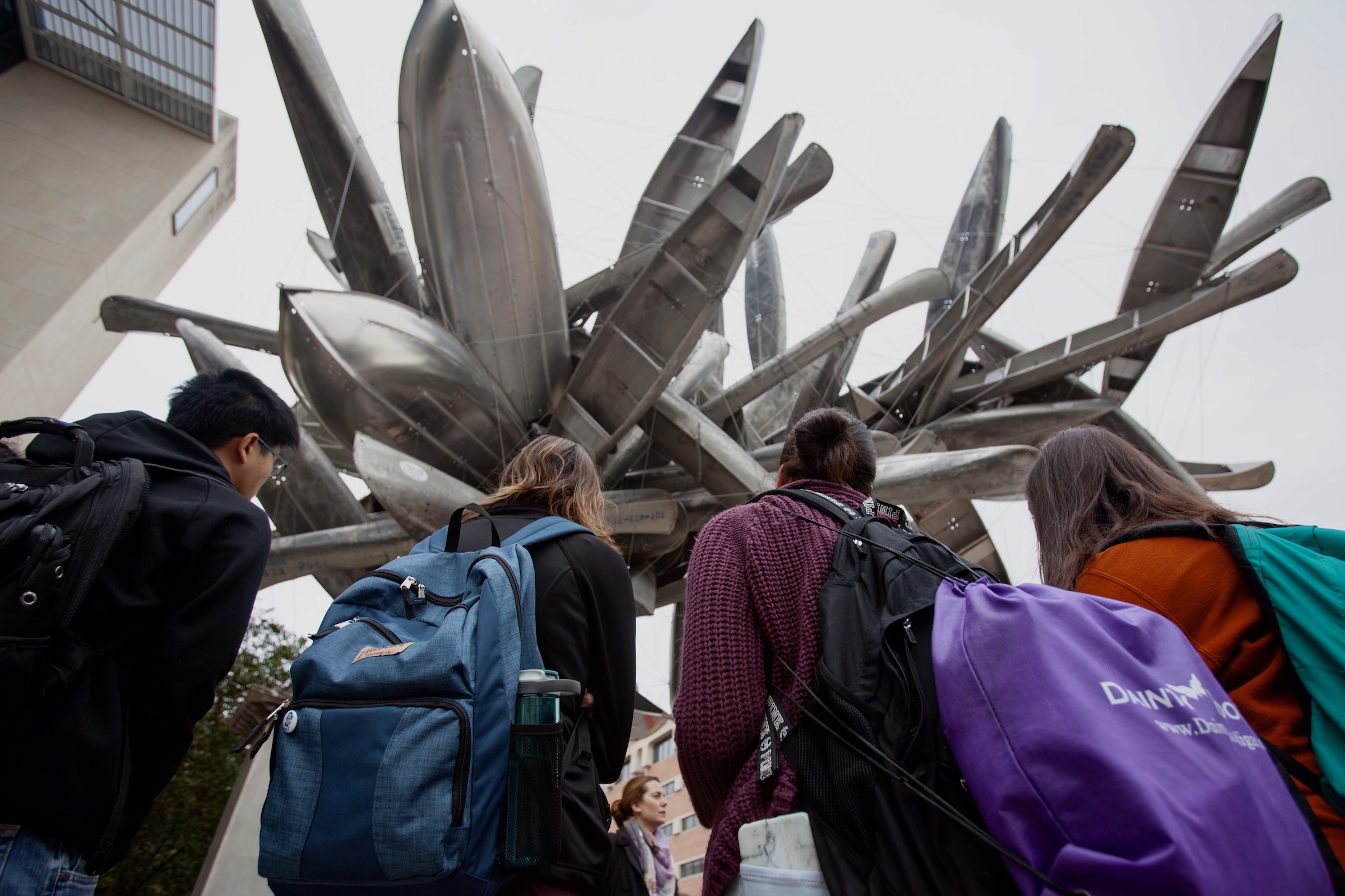 group of four students looking at an outdoor sculpture made of boats